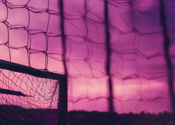 Abstract editorial hero image — silhouette of a goal net against a magenta and navy sky, mood of an upset breaking the title race wide open