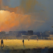 A painterly watercolour view of a small Northern English football ground at twilight with two floodlights lit and terraced rooftops behind